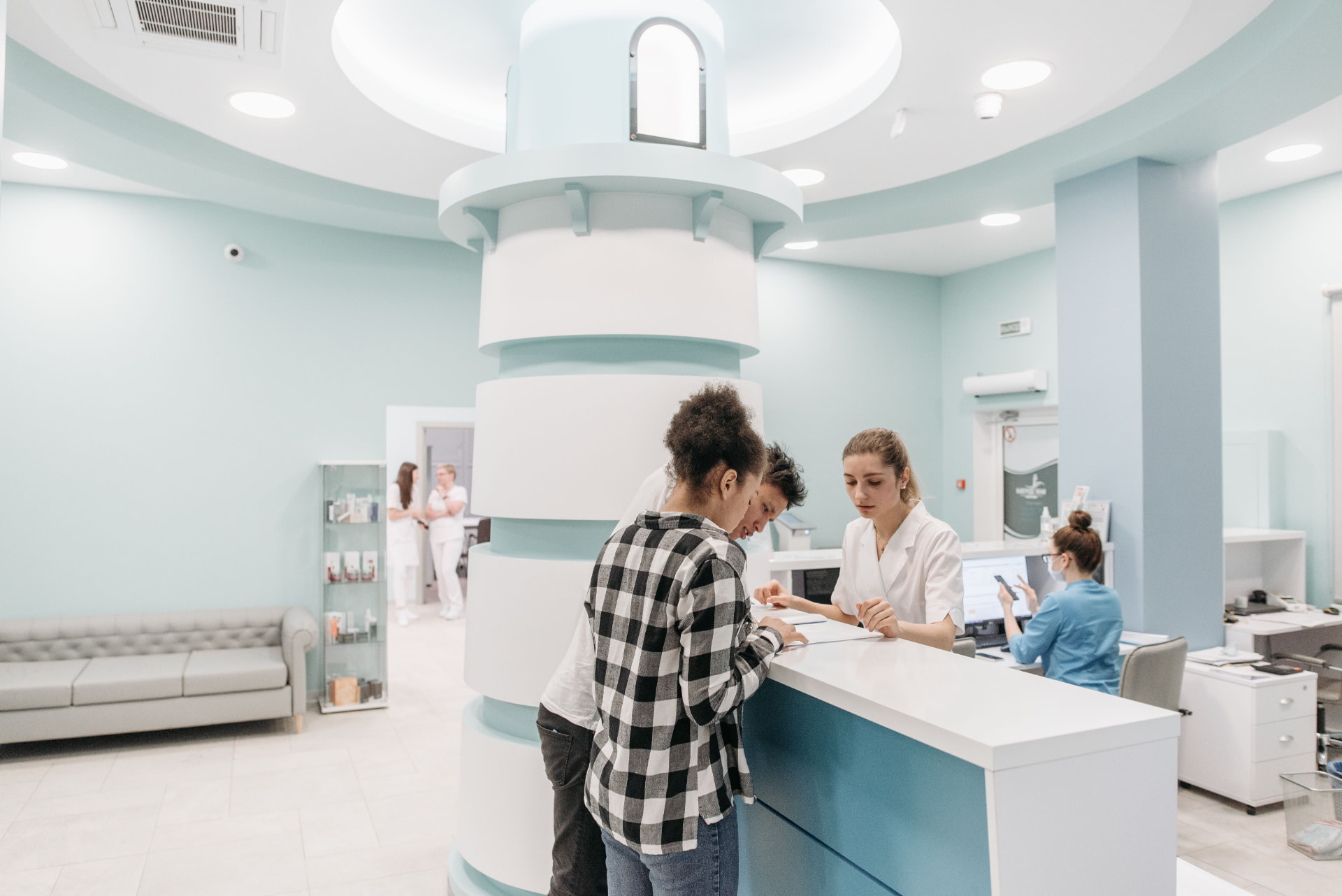 Patients checking in with staff at a healthcare clinic reception desk, illustrating patient acquisition covered in Proactive Marketing reviews